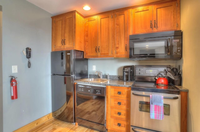 kitchen featuring dark stone counters, black appliances, sink, and light hardwood / wood-style flooring