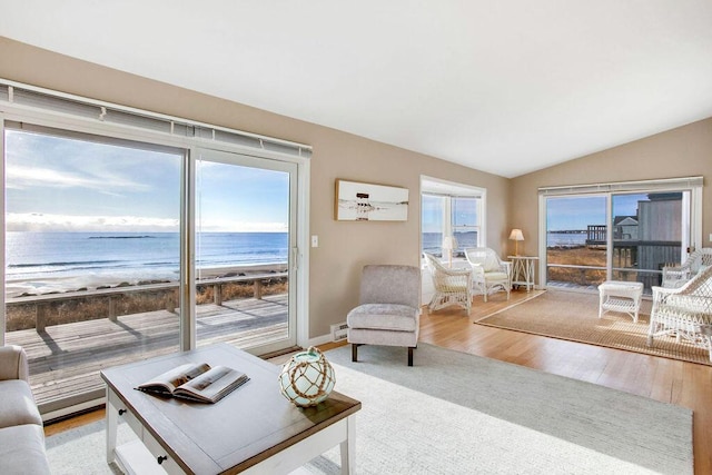 living room featuring a beach view, a water view, lofted ceiling, and light wood-type flooring