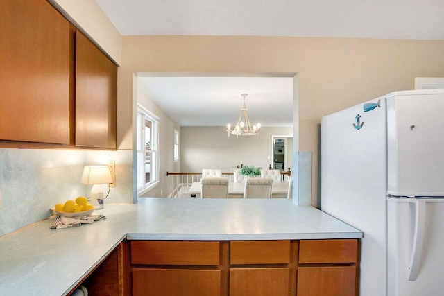 kitchen featuring hanging light fixtures, decorative backsplash, white fridge, kitchen peninsula, and a chandelier