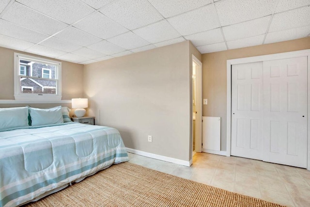 bedroom with a paneled ceiling, a closet, and light tile patterned floors