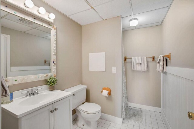 bathroom featuring tile patterned flooring, vanity, toilet, and a drop ceiling