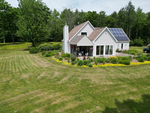 rear view of property featuring a lawn and solar panels