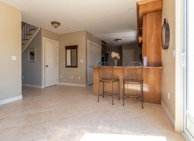 kitchen with black refrigerator, kitchen peninsula, a breakfast bar area, and light tile patterned flooring