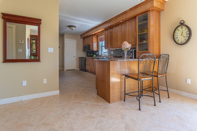 kitchen featuring stove, kitchen peninsula, a kitchen bar, sink, and light tile patterned floors