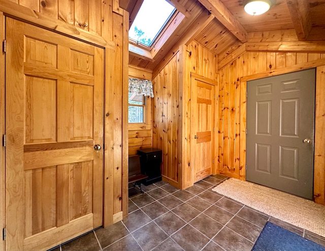 foyer featuring wooden walls, dark tile patterned flooring, wooden ceiling, and vaulted ceiling with skylight