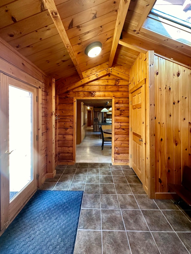 hall with dark tile patterned flooring, wooden walls, lofted ceiling with skylight, and wooden ceiling