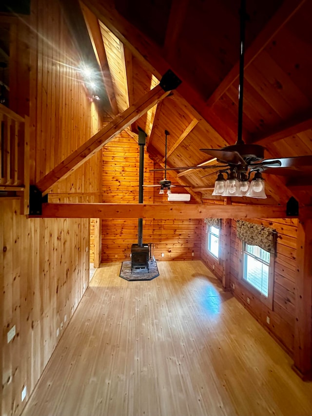 unfurnished living room with ceiling fan, vaulted ceiling with beams, wooden walls, and hardwood / wood-style flooring