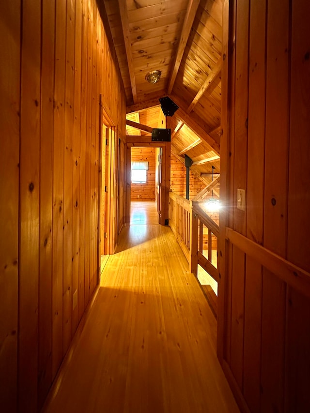 hallway with wood walls, light hardwood / wood-style floors, wooden ceiling, and vaulted ceiling with beams