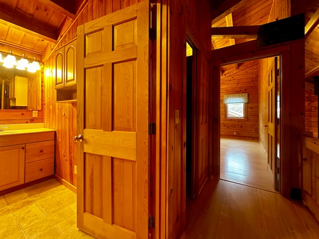 corridor featuring light wood-type flooring, wood ceiling, sink, vaulted ceiling with beams, and wood walls