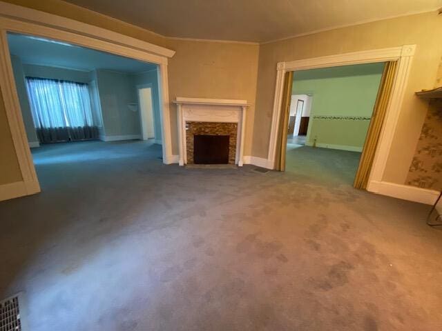 unfurnished living room with crown molding, a stone fireplace, and dark colored carpet