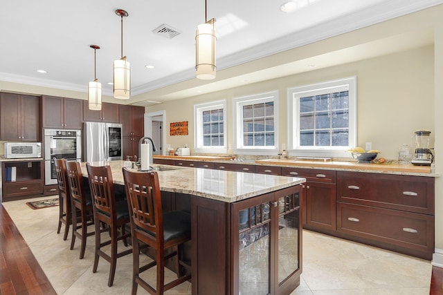 kitchen with a breakfast bar, decorative light fixtures, a kitchen island with sink, light stone counters, and stainless steel appliances