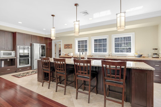 kitchen featuring pendant lighting, a center island, dark brown cabinetry, light stone counters, and stainless steel appliances