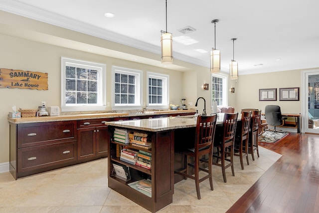 kitchen featuring light stone counters, sink, a kitchen island with sink, and hanging light fixtures