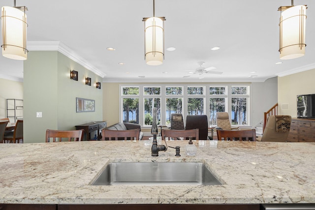 kitchen featuring crown molding, decorative light fixtures, light stone countertops, and a wealth of natural light