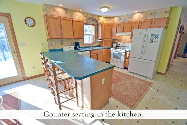 kitchen with a breakfast bar area, sink, kitchen peninsula, and white appliances