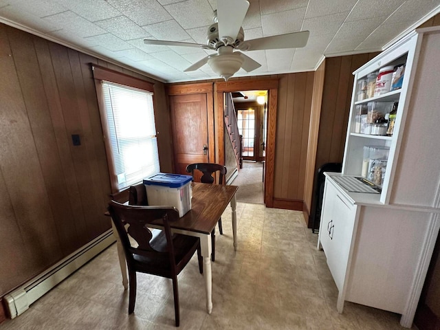 tiled dining room featuring ceiling fan, wooden walls, and a baseboard heating unit