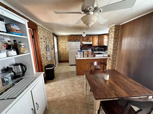 kitchen featuring crown molding, brick wall, white fridge, light tile floors, and ceiling fan
