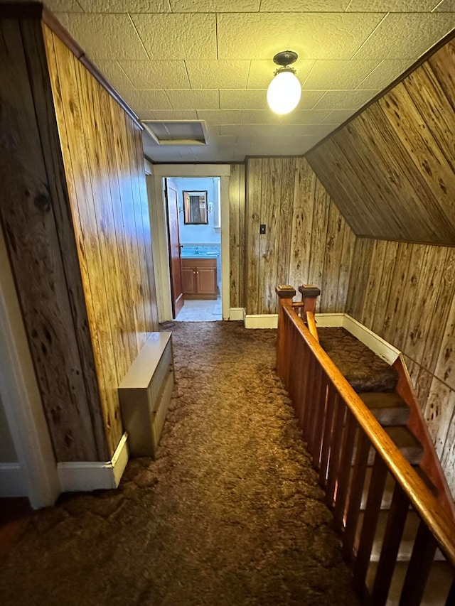 corridor with vaulted ceiling, wood walls, and dark carpet