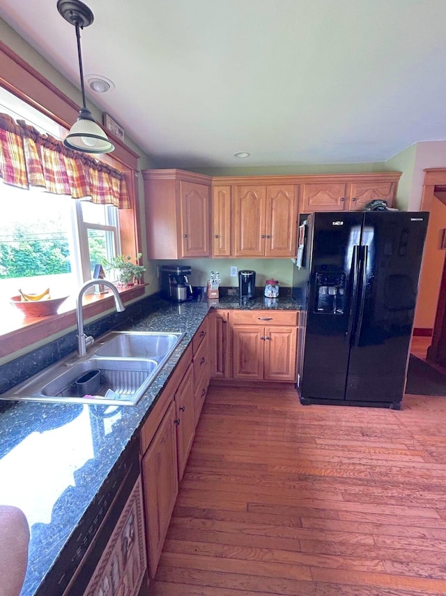 kitchen featuring wood-type flooring, hanging light fixtures, black fridge, sink, and dark stone countertops