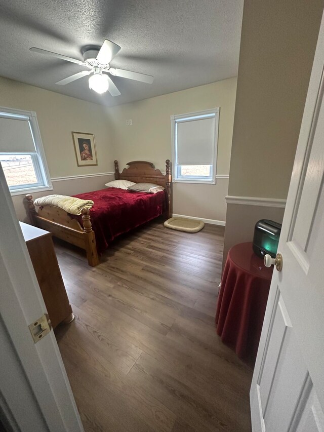 bedroom with a textured ceiling, ceiling fan, and dark wood-type flooring