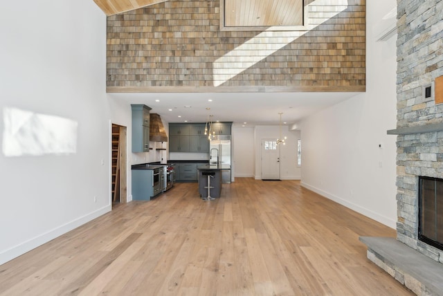 unfurnished living room featuring sink, an inviting chandelier, high vaulted ceiling, light hardwood / wood-style flooring, and a fireplace