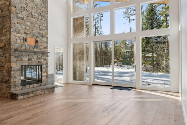 unfurnished living room with a stone fireplace, plenty of natural light, light wood-type flooring, and a towering ceiling