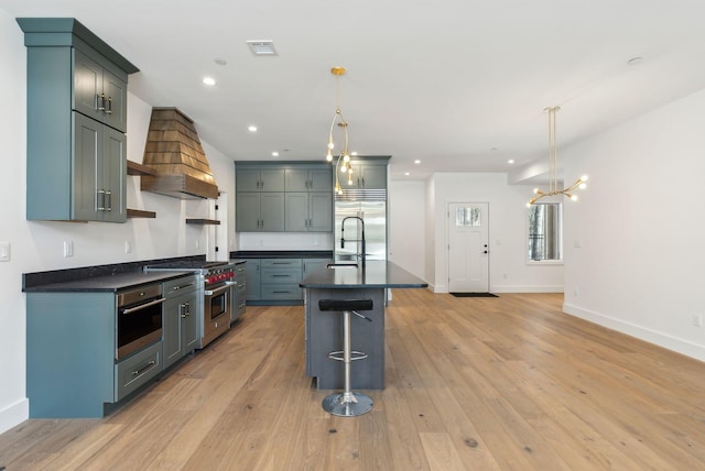 kitchen with hanging light fixtures, high end appliances, premium range hood, and an island with sink