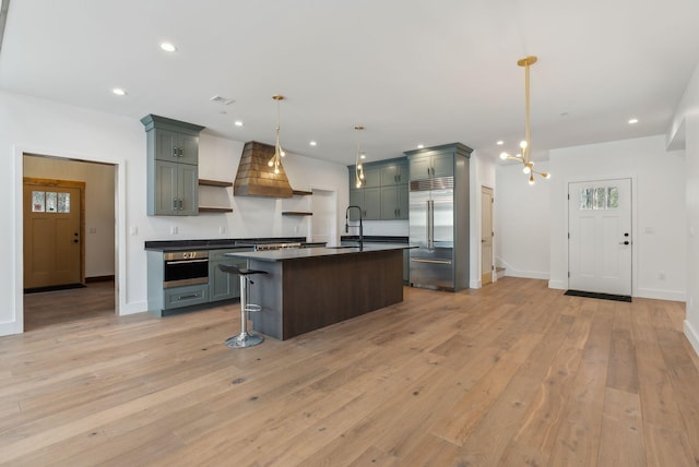 kitchen with a breakfast bar area, hanging light fixtures, appliances with stainless steel finishes, an island with sink, and light hardwood / wood-style floors