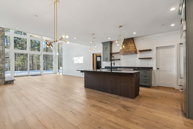 kitchen featuring decorative light fixtures, sink, custom exhaust hood, a center island with sink, and light wood-type flooring