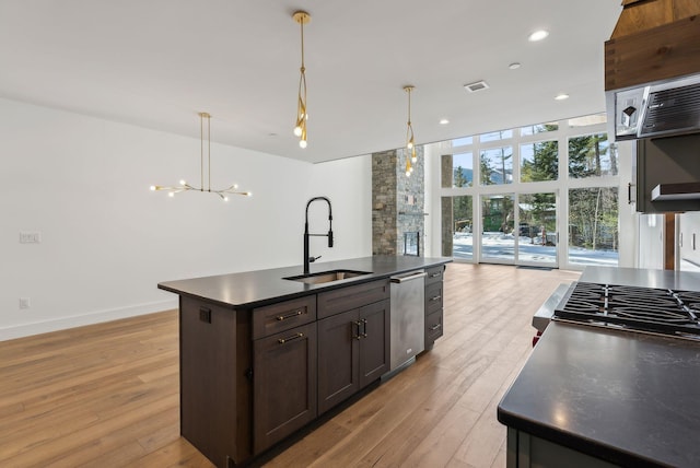 kitchen with hanging light fixtures, sink, a center island with sink, and light wood-type flooring