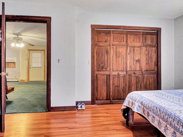 bedroom with ceiling fan, a textured ceiling, light carpet, baseboard heating, and a closet