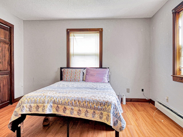 bedroom with light hardwood / wood-style floors, a baseboard heating unit, and a textured ceiling