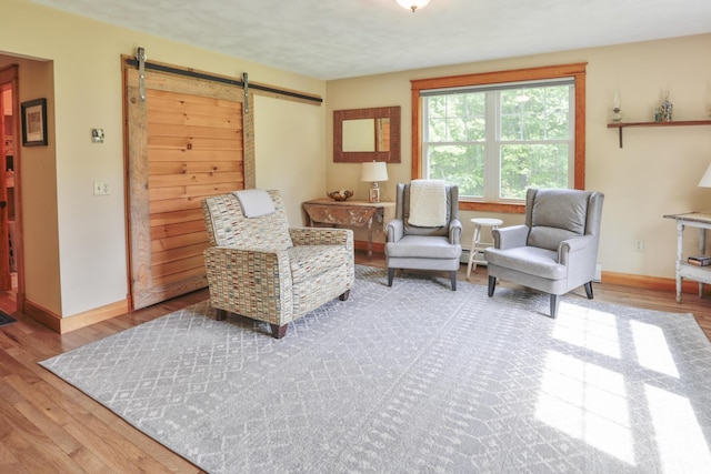 sitting room with a barn door, light hardwood / wood-style flooring, and a baseboard heating unit