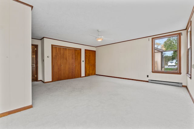 unfurnished bedroom with ceiling fan, multiple closets, baseboard heating, carpet floors, and ornamental molding