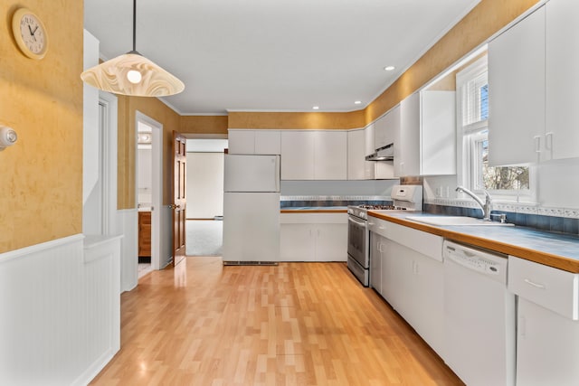 kitchen with white cabinets, sink, white appliances, hanging light fixtures, and light hardwood / wood-style flooring