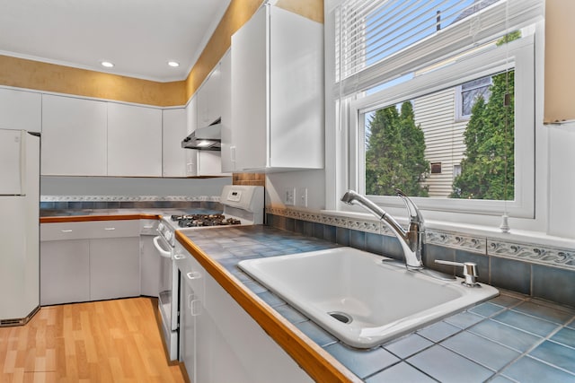 kitchen with sink, white appliances, white cabinetry, light hardwood / wood-style flooring, and tile counters