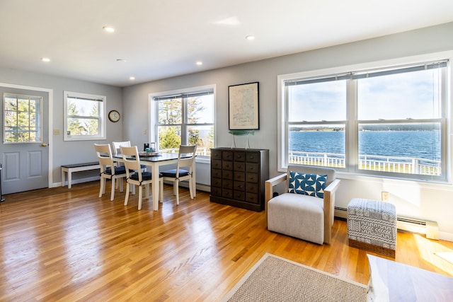 dining area with a baseboard heating unit, light hardwood / wood-style floors, and a water view