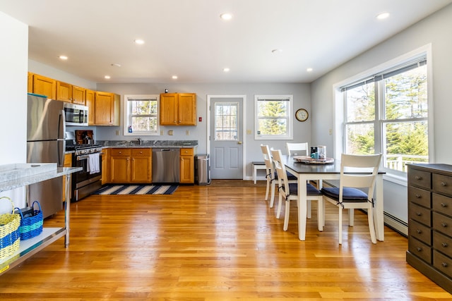 kitchen with appliances with stainless steel finishes, light hardwood / wood-style flooring, dark stone countertops, a baseboard radiator, and sink