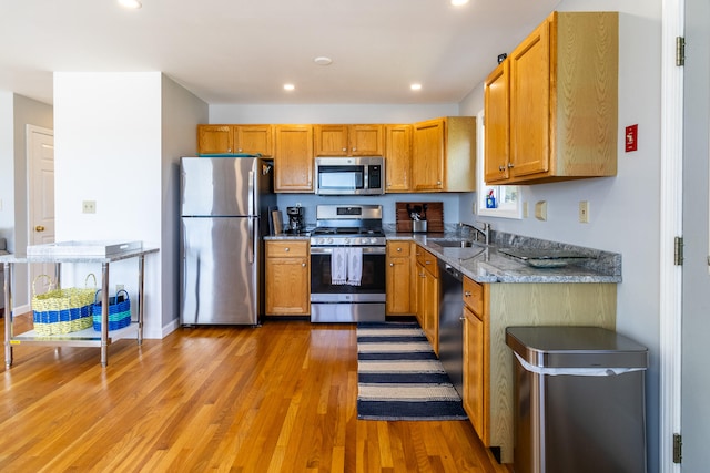 kitchen featuring light stone counters, appliances with stainless steel finishes, sink, and light wood-type flooring