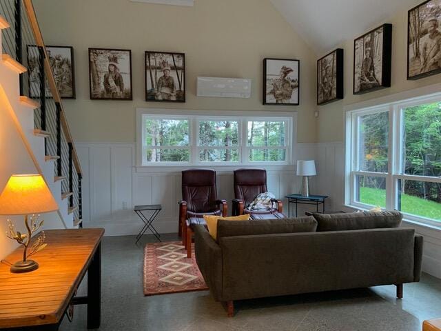 living room featuring high vaulted ceiling, stairway, wainscoting, and a decorative wall