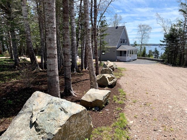 view of side of home with dirt driveway and roof with shingles