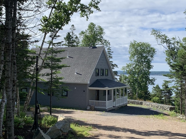 view of side of home featuring a porch, a water view, driveway, and a shingled roof