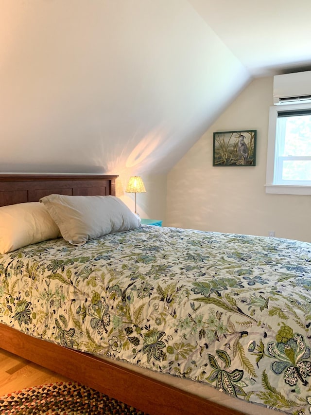 bedroom featuring lofted ceiling, an AC wall unit, and wood finished floors