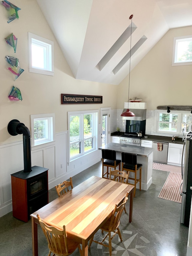 dining area with a wood stove, high vaulted ceiling, and wainscoting