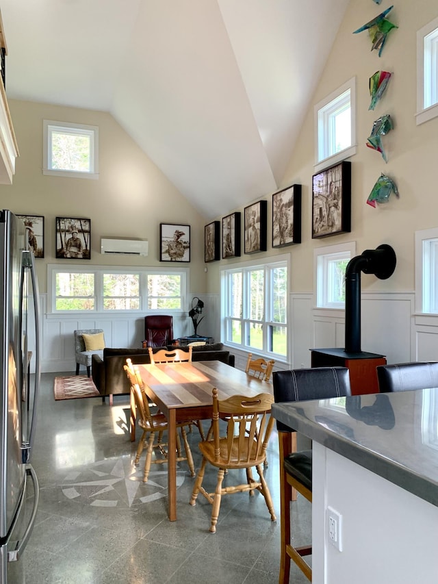 dining space with high vaulted ceiling, a wood stove, wainscoting, and granite finish floor