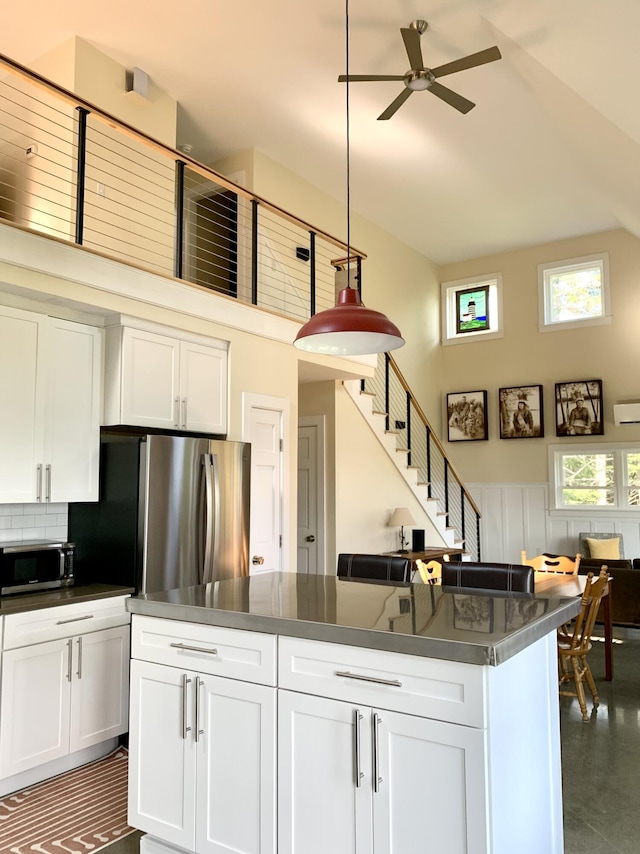 kitchen with appliances with stainless steel finishes, dark countertops, a towering ceiling, and white cabinets