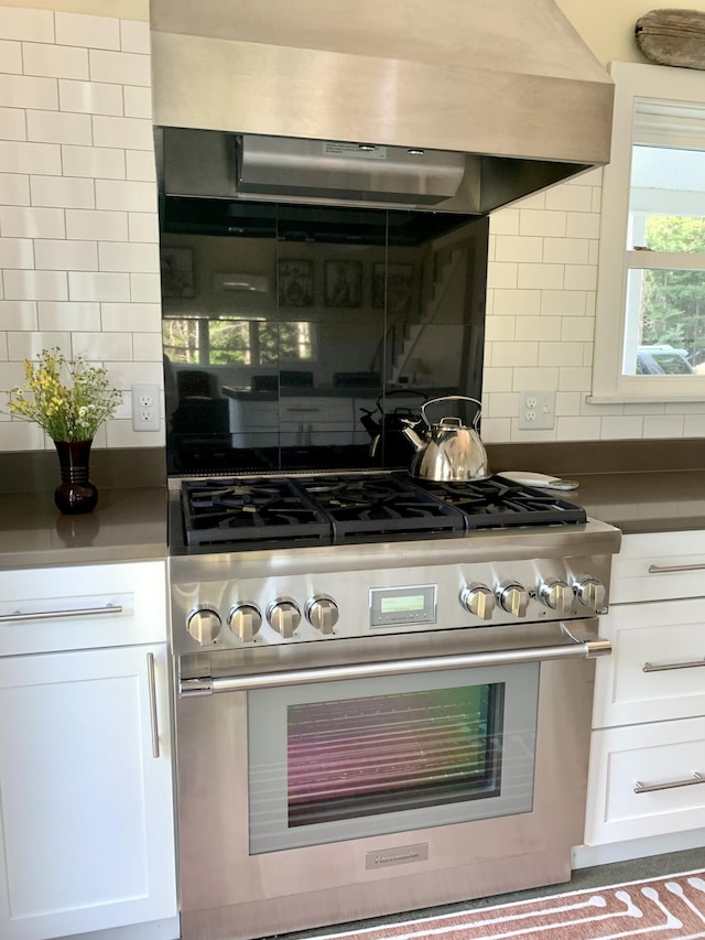 kitchen featuring stainless steel range, white cabinets, backsplash, and exhaust hood