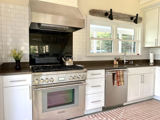 kitchen with dark countertops, backsplash, appliances with stainless steel finishes, a sink, and wall chimney exhaust hood