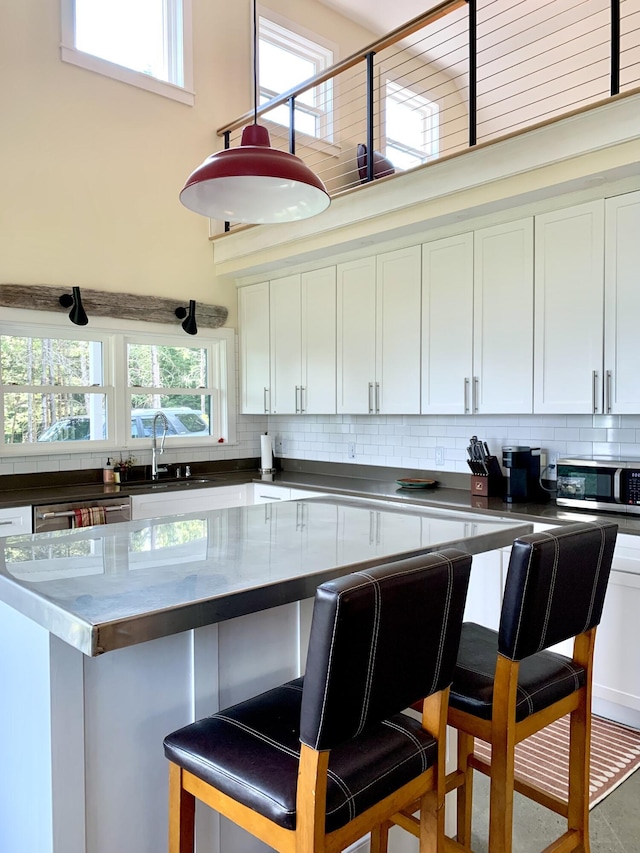 kitchen with a breakfast bar area, stainless steel appliances, dark countertops, decorative backsplash, and white cabinets