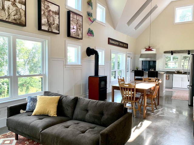 living area featuring a wainscoted wall, high vaulted ceiling, a wood stove, and a decorative wall